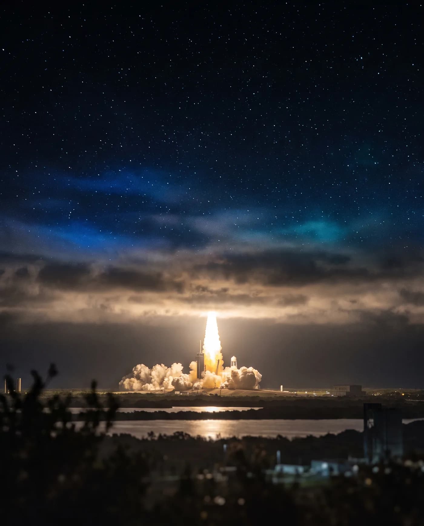 A rocket lifting off at night, its plume reflected on the water below.